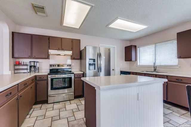 a kitchen with stainless steel appliances granite countertop a sink stove refrigerator and cabinets