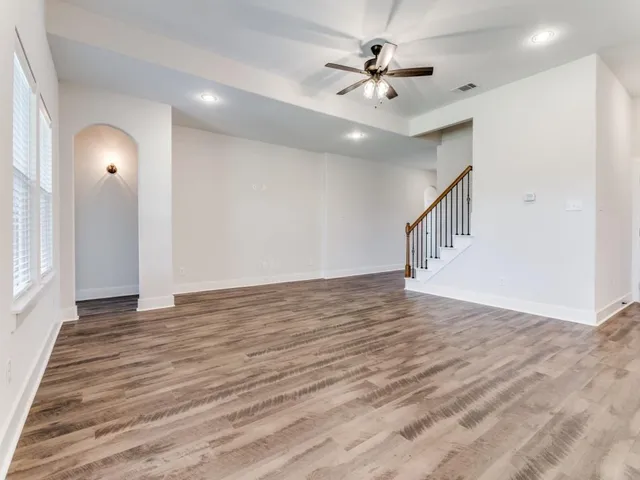 a view of an empty room with wooden floor and a ceiling fan