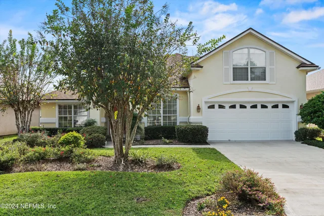 a view of a white house with a big yard and potted plants and large trees