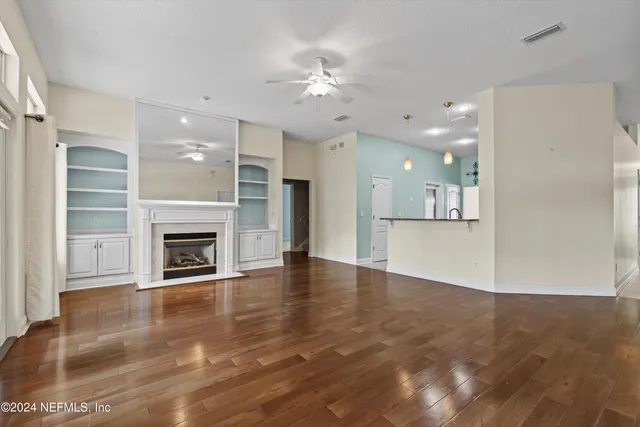 a view of a livingroom with a fireplace a ceiling fan and kitchen space