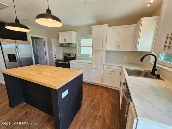 a kitchen with kitchen island a sink a stove a refrigerator cabinets and living room view