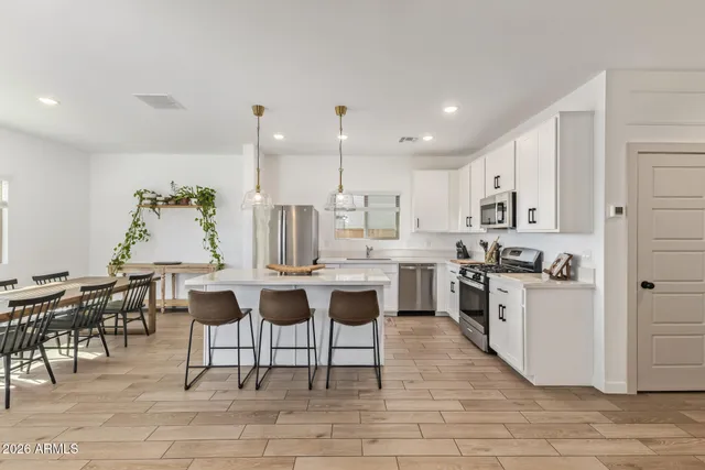 a open kitchen with stainless steel appliances kitchen island a white table chairs and a wooden floor