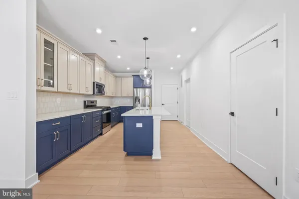a large kitchen with stainless steel appliances granite countertop a stove a sink a refrigerator and white cabinets with wooden floor