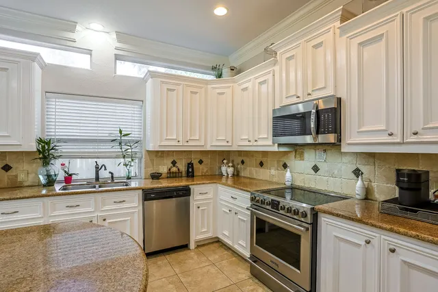 a kitchen with stainless steel appliances granite countertop white cabinets a sink a stove a window and dishwasher