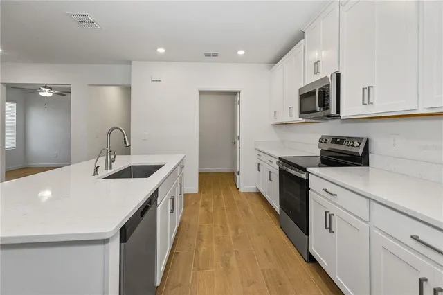 a kitchen with stainless steel appliances granite countertop a sink a stove top oven a refrigerator with white cabinets and wooden floor