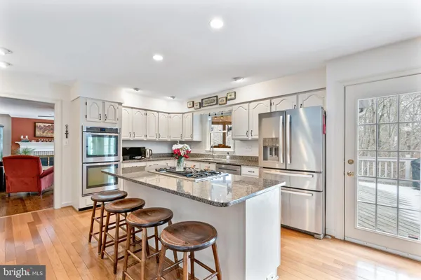 a kitchen with stainless steel appliances granite countertop a refrigerator a stove a sink a dining table and chairs with wooden floor