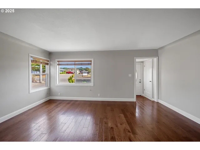 a view of an empty room with window and wooden floor