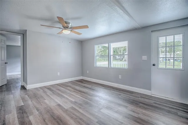 an empty room with wooden floor ceiling fan and windows