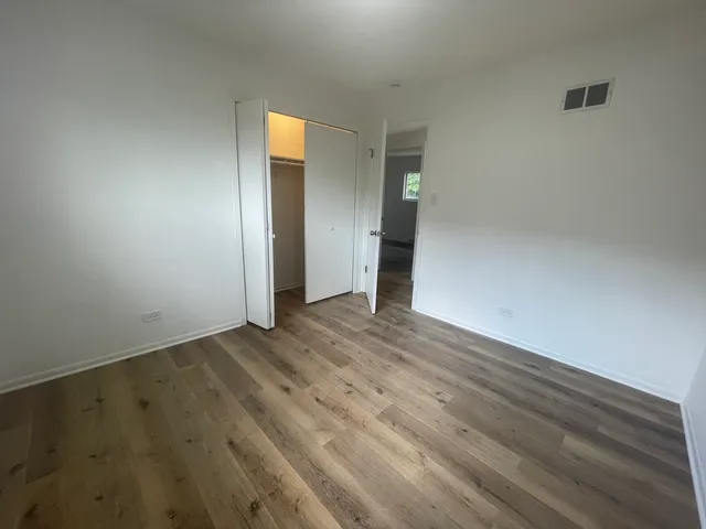 a view of an empty room with wooden floor and closet