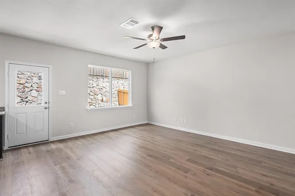 an empty room with wooden floor chandelier fan and windows