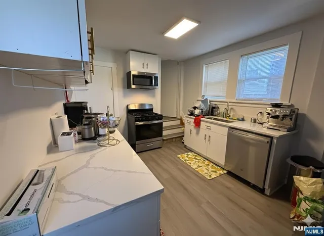 a kitchen with stainless steel appliances a stove top oven a sink a refrigerator white cabinets and wooden floor