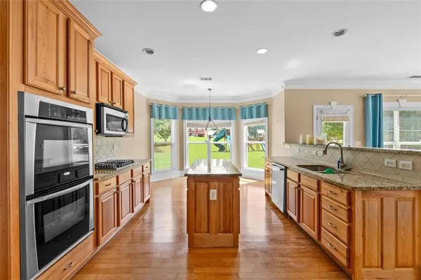 a kitchen with stainless steel appliances granite countertop a stove a sink and a refrigerator with wooden floor