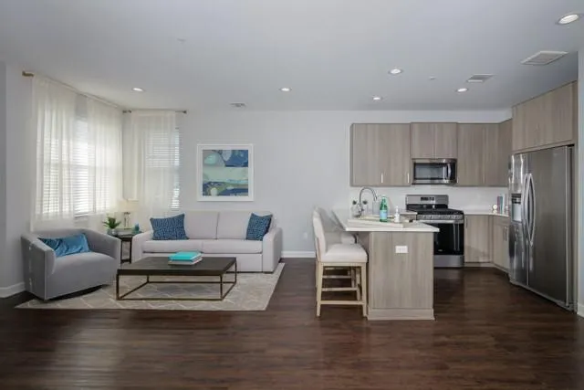 a living room with stainless steel appliances kitchen island granite countertop a stove a sink a refrigerator and a couch