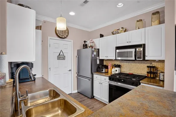 a kitchen with granite countertop a refrigerator a stove a sink and white cabinets with wooden floor