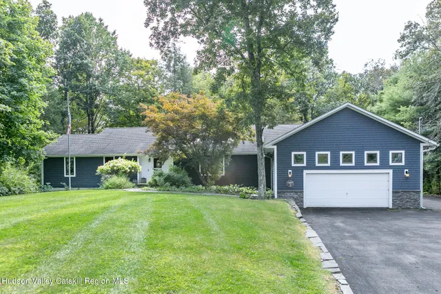 a house that is sitting in the grass with large trees and plants
