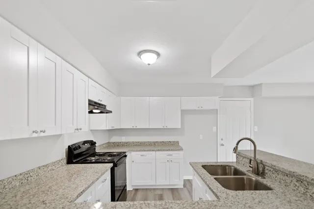 a kitchen with granite countertop a sink a stove and cabinets