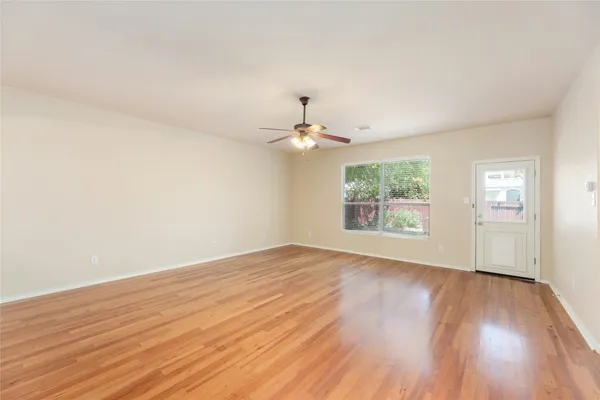 an empty room with wooden floor chandelier fan and windows