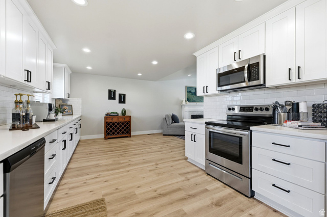 1405 Vintry Lane Murray, UT 84121 - Photo 15 of 44 Kitchen featuring white shaker-style cabinetry with black hardware, stainless steel appliances, white subway tile backsplash, and light wood-finish flooring