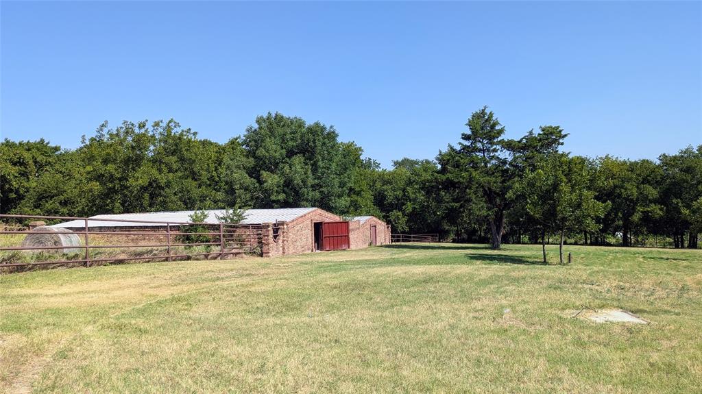 1431 South Houston School Road Lancaster, TX 75146 - Photo 39 of 39 Expansive grassy field with mature trees and a brick-sided outbuilding featuring a metal roof and red barn doors