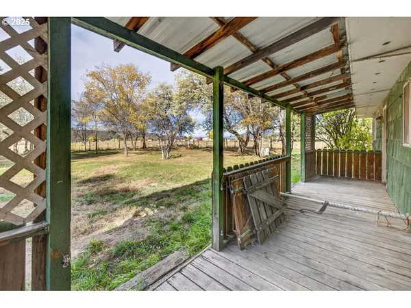 a view of a porch with wooden floor in front of a house with a yard