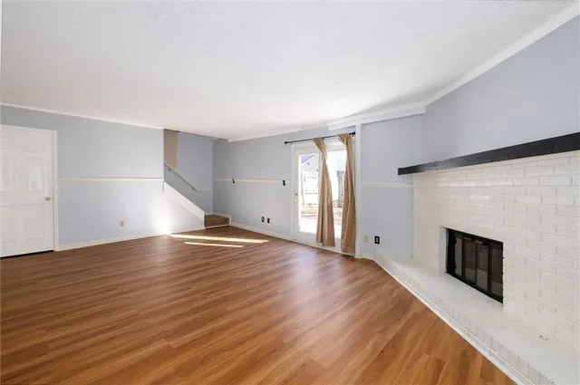 an empty room with wooden floor fireplace and windows