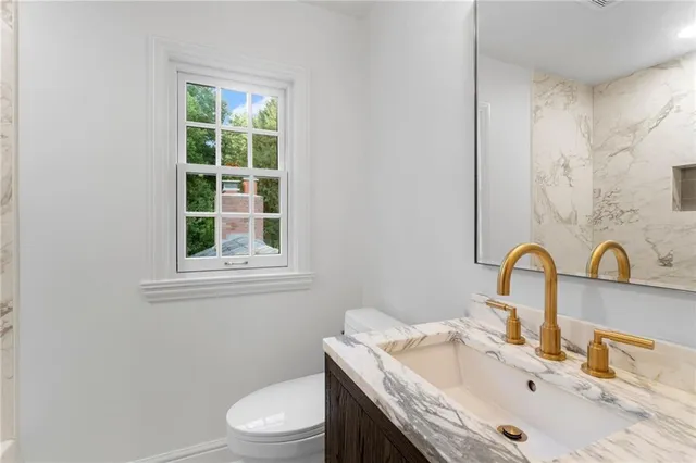 a bathroom with a granite countertop sink a toilet and a window