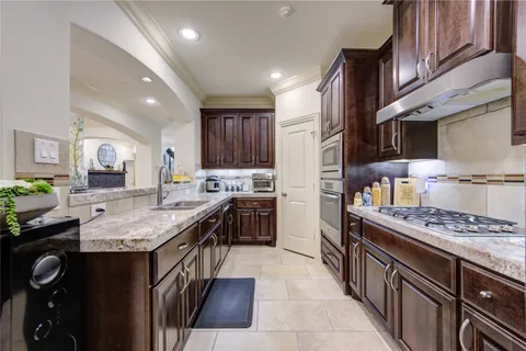 a kitchen with stainless steel appliances granite countertop a stove top oven a sink dishwasher and a refrigerator with wooden cabinets