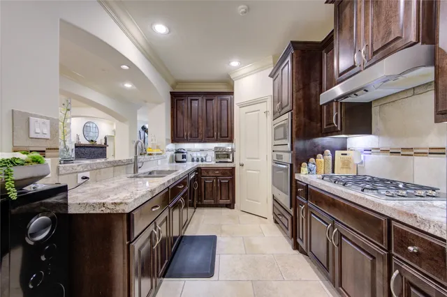 a kitchen with stainless steel appliances granite countertop a stove top oven a sink dishwasher and a refrigerator with wooden cabinets