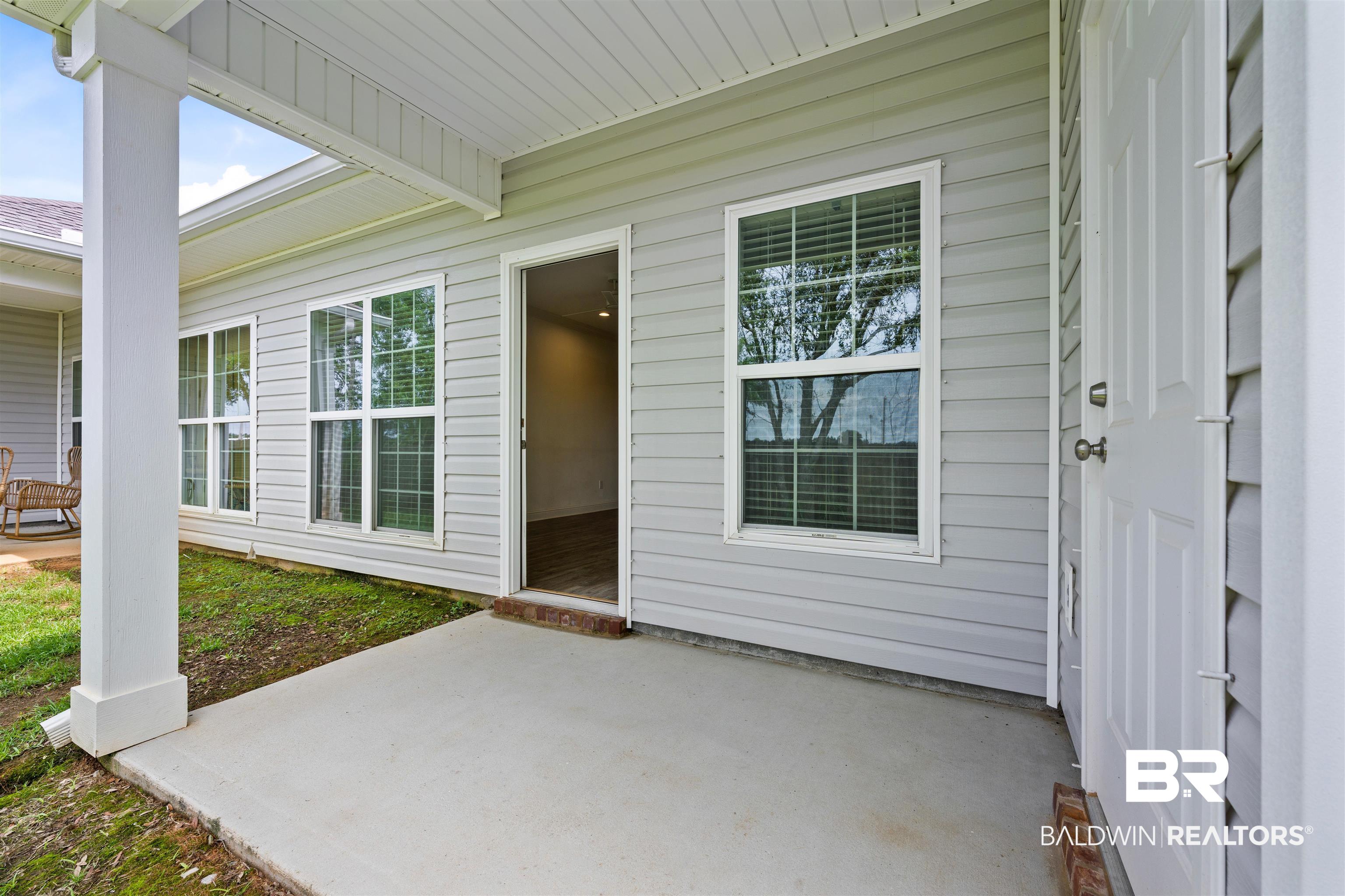 2651 South Juniper Street, Unit 1801 Foley, AL 36535 - Photo 15 of 16 Covered concrete patio with white vinyl siding, multiple windows with venetian blinds, and a white paneled door