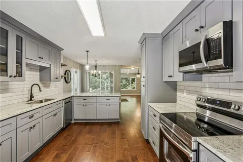 a kitchen with stainless steel appliances granite countertop a stove top oven a sink dishwasher and white cabinets with wooden floor