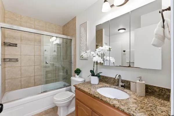 a bathroom with a granite countertop sink a toilet a mirror a bathtub and shower