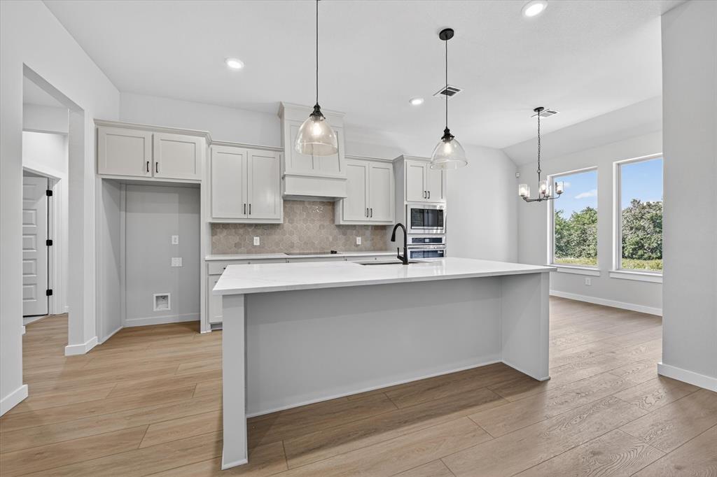 409 Mcalpine Springtown, TX 76082 - Photo 13 of 38 Open-concept kitchen featuring a large central island with a solid surface countertop, white shaker cabinetry, a geometric tile backsplash, and wood-finish flooring