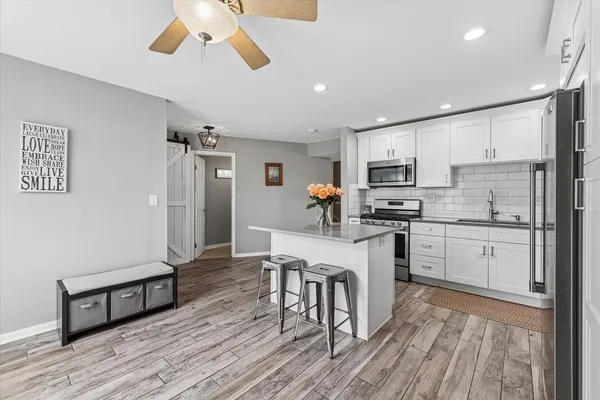 a kitchen with a refrigerator a white stove top oven a dining table and chairs with wooden floor