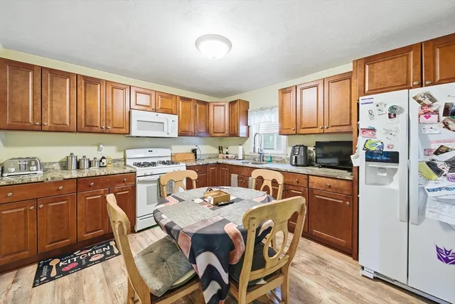 a kitchen with stainless steel appliances granite countertop a refrigerator a sink dishwasher a dining table and chairs with wooden floor