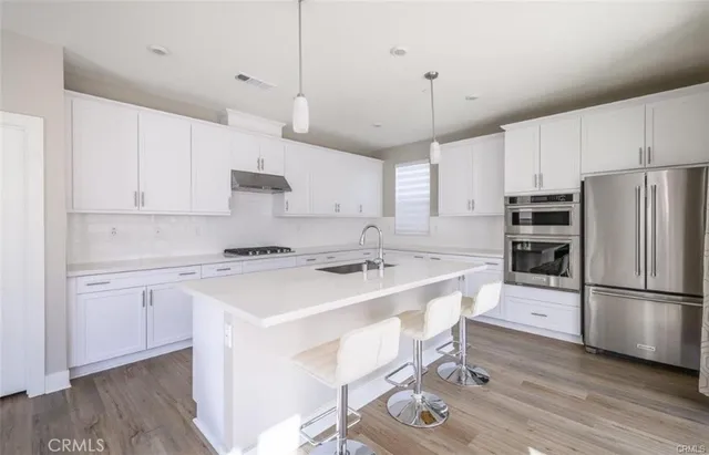 a kitchen with stainless steel appliances granite countertop a sink a stove a refrigerator and island with wooden floor