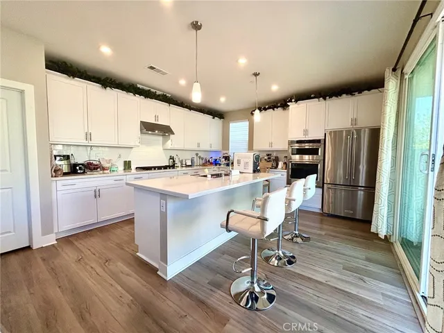 a kitchen with stainless steel appliances kitchen island granite countertop a refrigerator a stove top oven a sink dishwasher and white cabinets with wooden floor