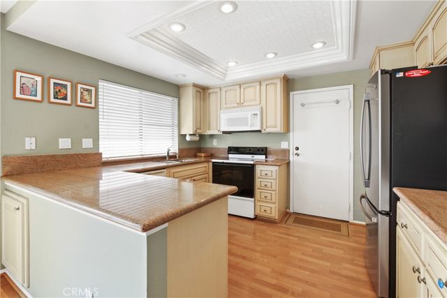 a kitchen with granite countertop a refrigerator a stove a sink dishwasher and white countertops with wooden floor