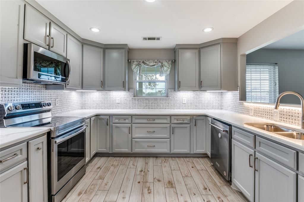155 Smith Lane Combine, TX 75159 - Photo 3 of 31 Kitchen with gray cabinets, appliances with stainless steel finishes, tasteful backsplash, light stone counters, and light wood-style flooring