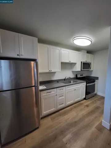 a kitchen with granite countertop a refrigerator a sink dishwasher a stove and white cabinets next to a window