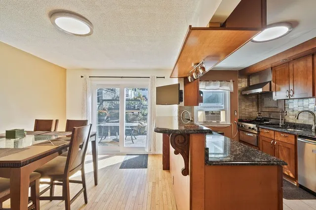 a kitchen with stainless steel appliances granite countertop a stove top oven a sink a dining table and chairs with wooden floor