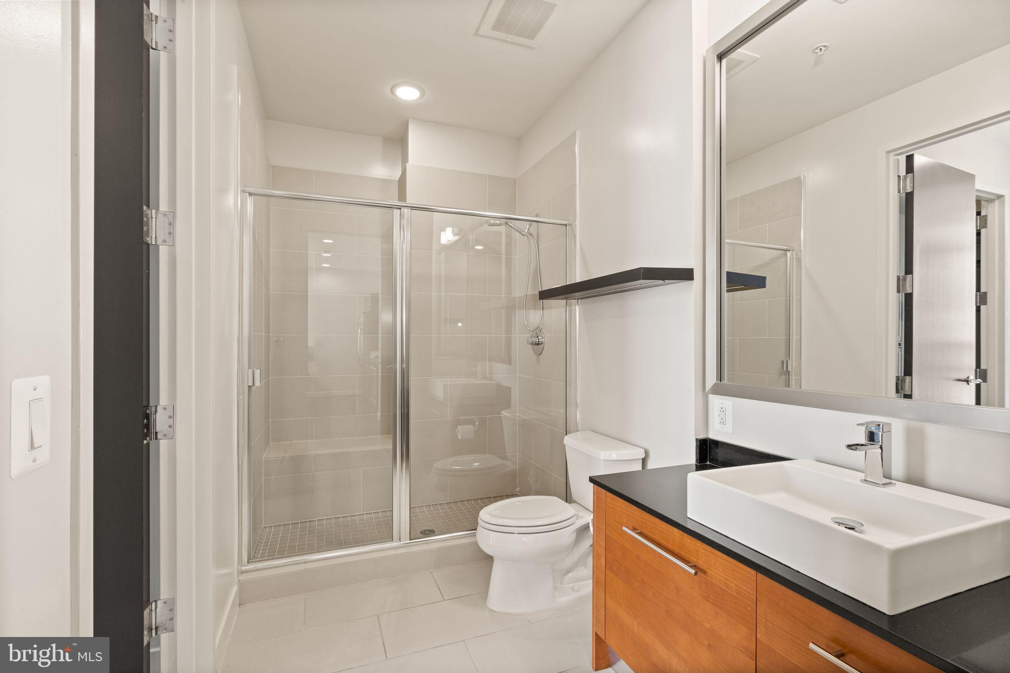 12025 New Dominion Parkway, Unit 406 Reston, VA 20190 - Photo 26 of 31 a bathroom with a sink toilet a mirror and shower