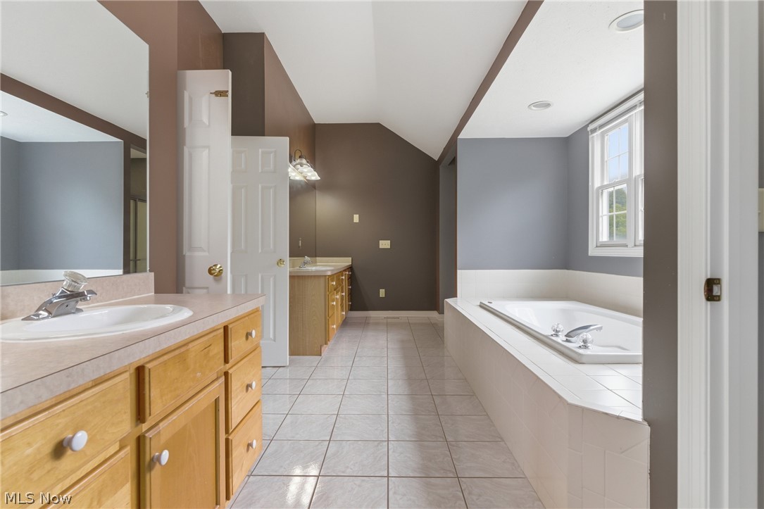 11678 Dunham Road Northfield, OH 44067 - Photo 21 of 38 Expansive bathroom featuring dual vanity cabinets with integrated sinks, a built-in soaking tub, a large framed mirror, and tiled flooring