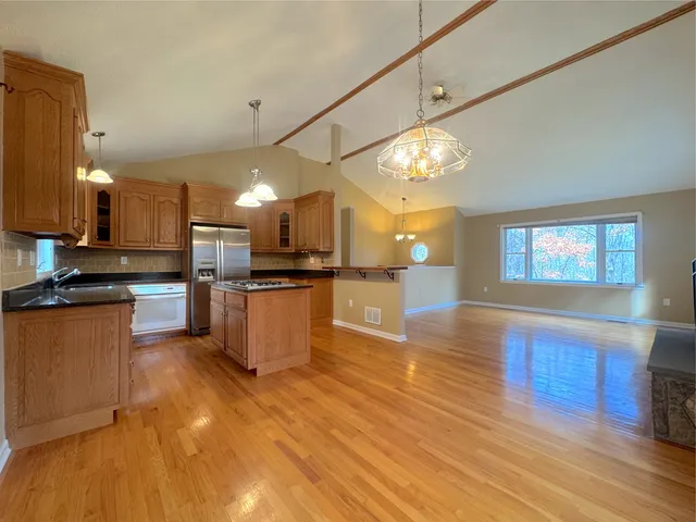 a kitchen with stainless steel appliances kitchen island granite countertop a stove a refrigerator a sink dishwasher and a fireplace with wooden floor