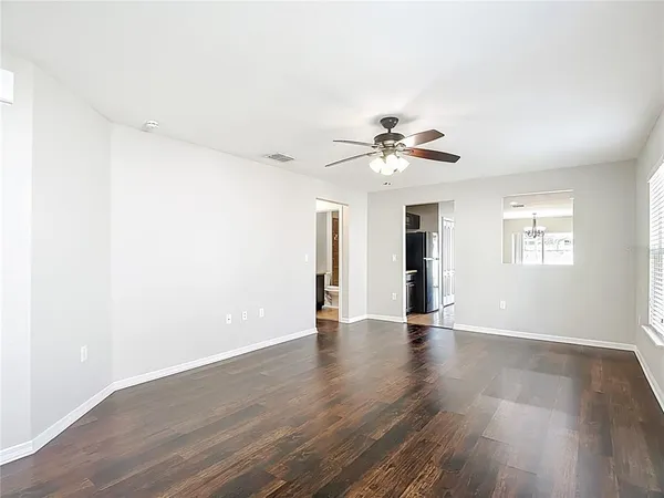 an empty room with wooden floor chandelier fan and windows