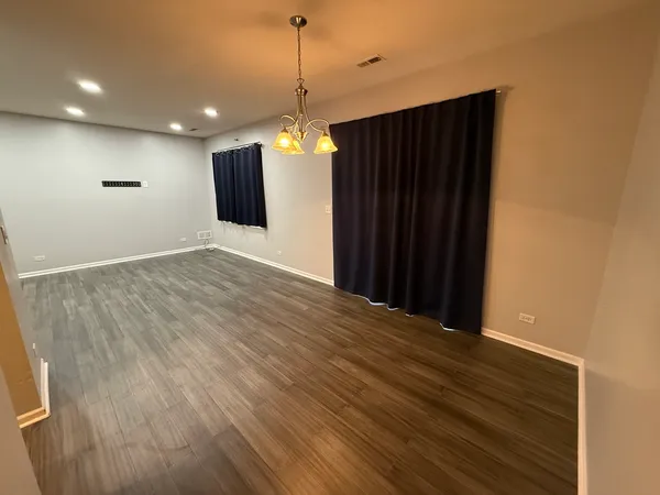 a view of an empty room with wooden floor and a ceiling fan