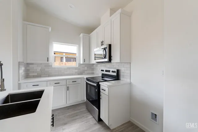 a kitchen with stainless steel appliances granite countertop a stove a sink and white cabinets