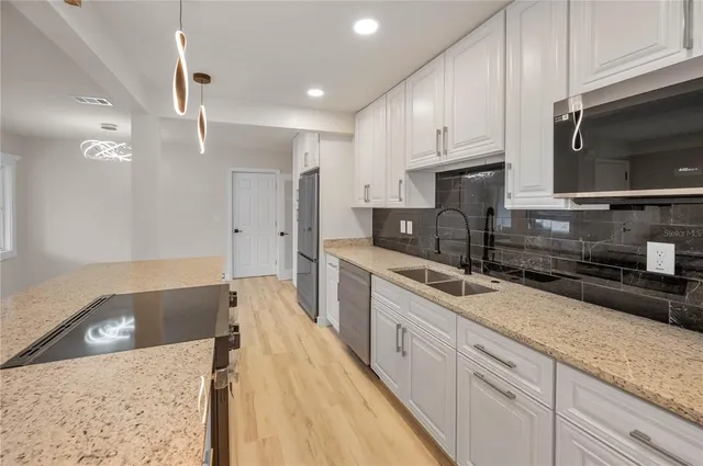 a large kitchen with granite countertop a sink a counter space stainless steel appliances and cabinets