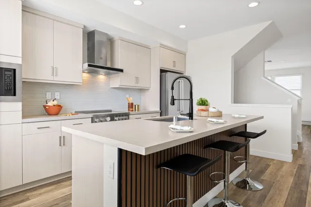 a kitchen with stainless steel appliances a sink a stove and white cabinets with wooden floor