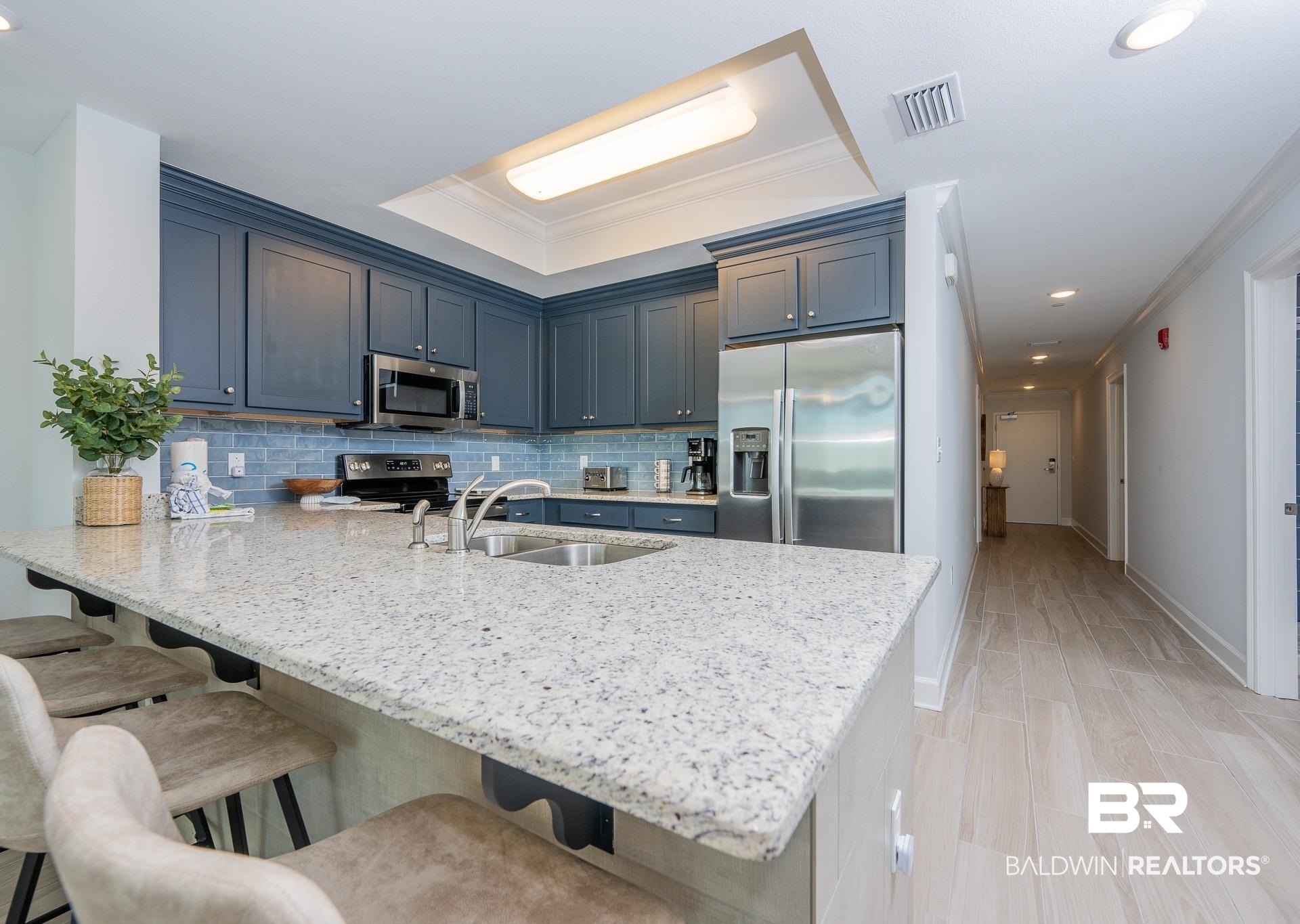 23008 Perdido Beach Boulevard, Unit 506 Orange Beach, AL 36561 - Photo 4 of 48 Kitchen featuring appliances with stainless steel finishes, a peninsula, a tray ceiling, visible vents, and ornamental molding