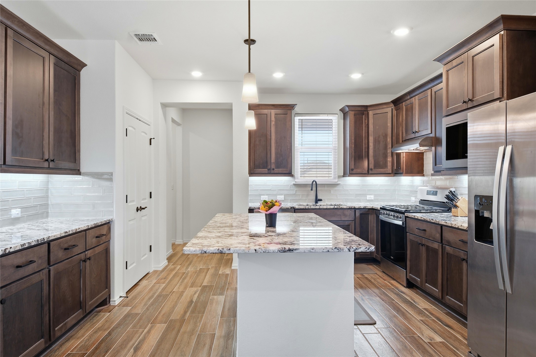 122 Clay Hl Street Georgetown, TX 78633 - Photo 6 of 31 Kitchen featuring stainless steel appliances, light stone countertops, a kitchen island, wood tiled floors, and pendant lighting